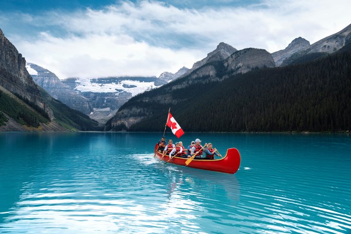 Group of people in a red canoe on the turquoise blue Lake Louise, with a Canadian flag on the canoe.