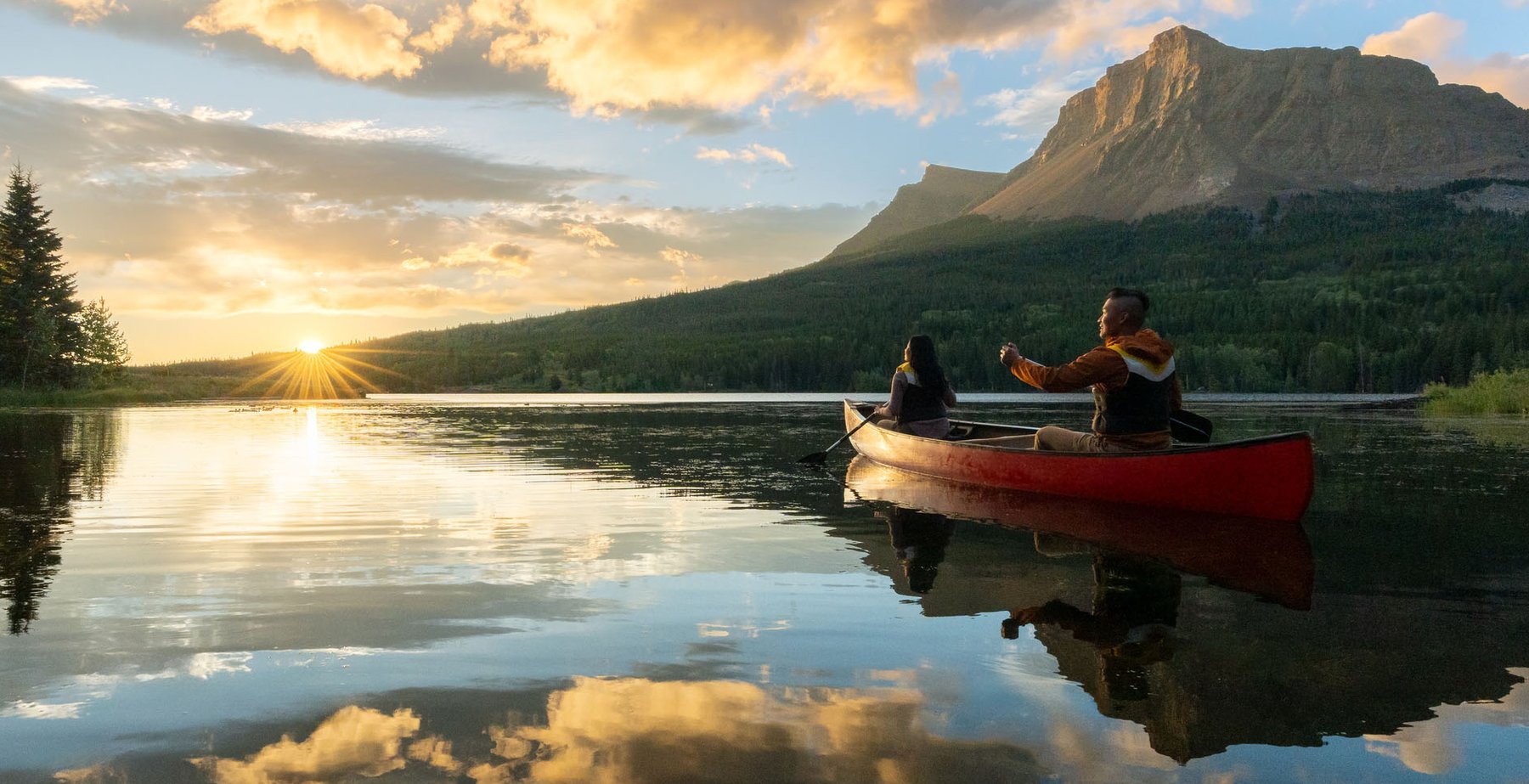 A couple goes out on a canoe at Glamping Resorts in Castle Provincial Park during a fiery sunrise.