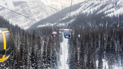 A gondola going up its track in the snow covered mountains.