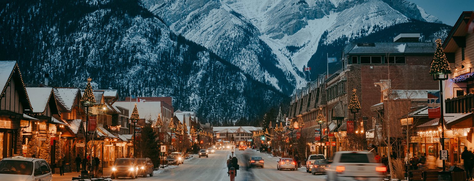 An idyllic winter moment on Banff Avenue at dusk, with shops lining either side of a street that seems to lead toward a mountain.