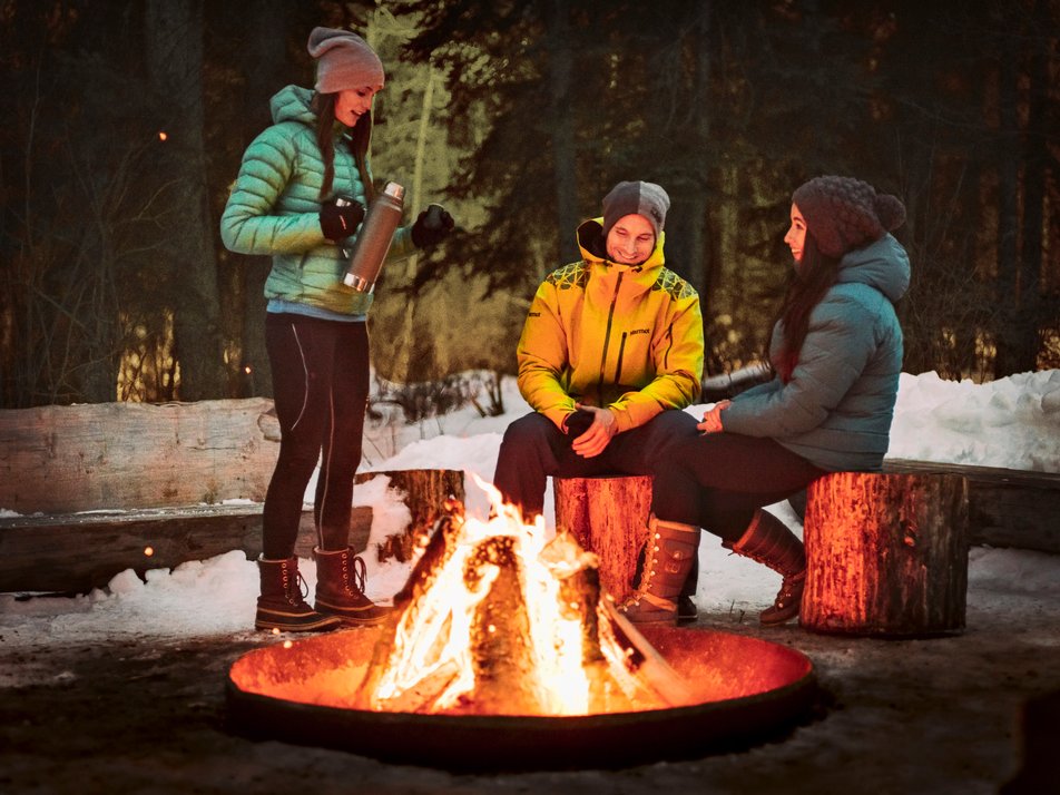 Friends having a hot drink around a campfire at night.