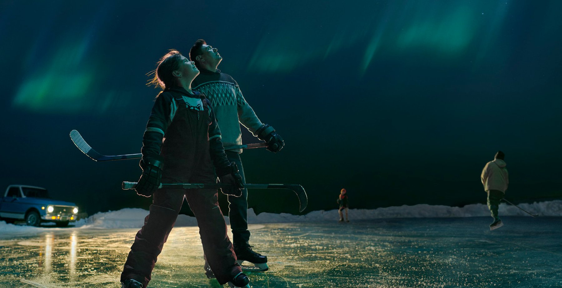 Hockey coach and player pausing from playing pond hockey to look up and admire the northern lights overhead.