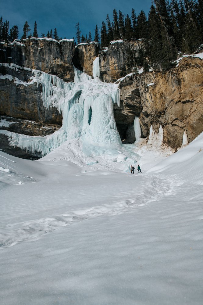 Couple winter hiking in front of the frozen waterfall of Panther Falls in Banff National Park