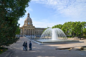 Group of people in a circle standing outside of a legislation building with a fountain in front.