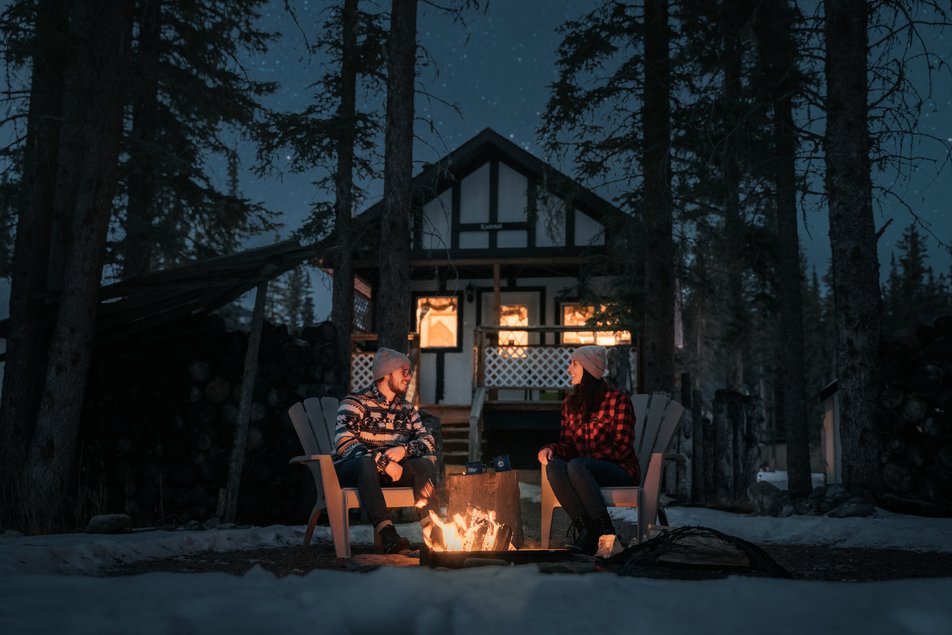 A couple sitting near a campfire in front of a cabin at Expanse Cottages.