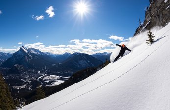 A snowboarder carves and creates a snow spray while snowboarding at Mount Norquay Ski Resort.
