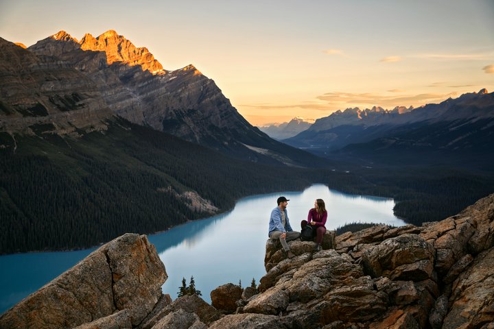 Two people sitting on a rock overlooking Peyto Lake at sunrise.