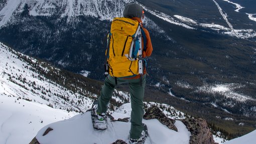 A person wearing snowshoes standing on a rock over looking the mountain view and valley below.