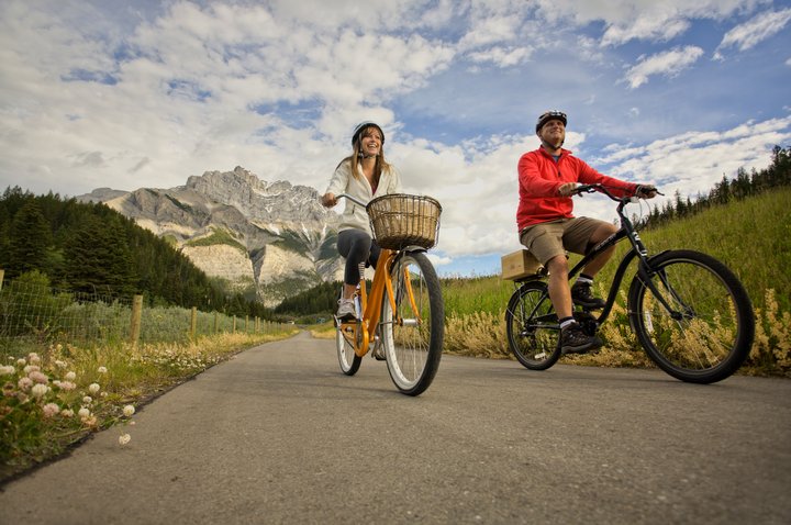Couple bike riding along a pathway with mountains in the background