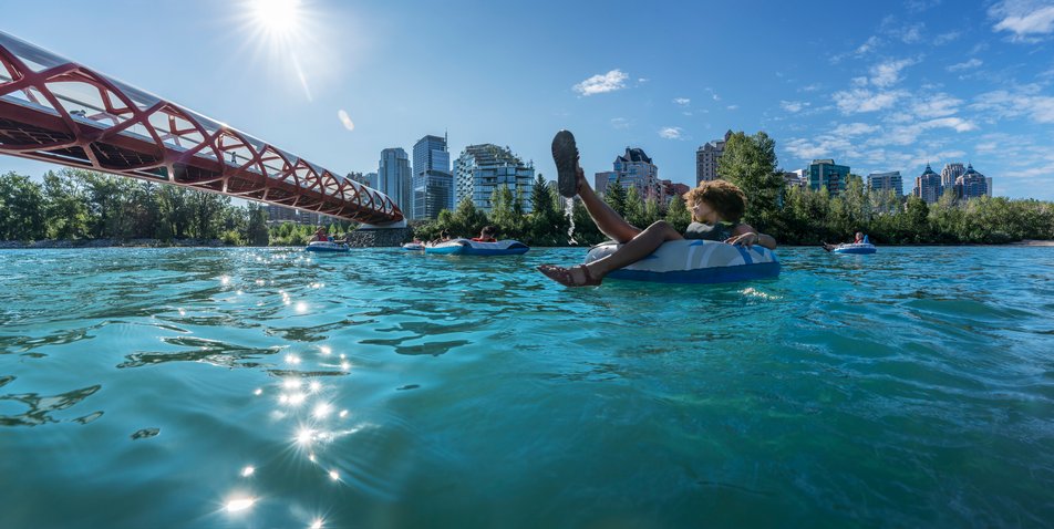 People floating down the Bow River in Calgary with the Peace Bridge and city skyline in the background.