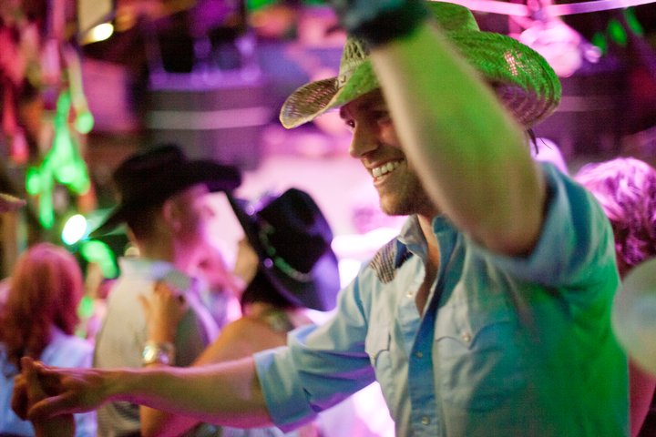 Close up of a man wearing a cowboy hat dancing in a country bar
