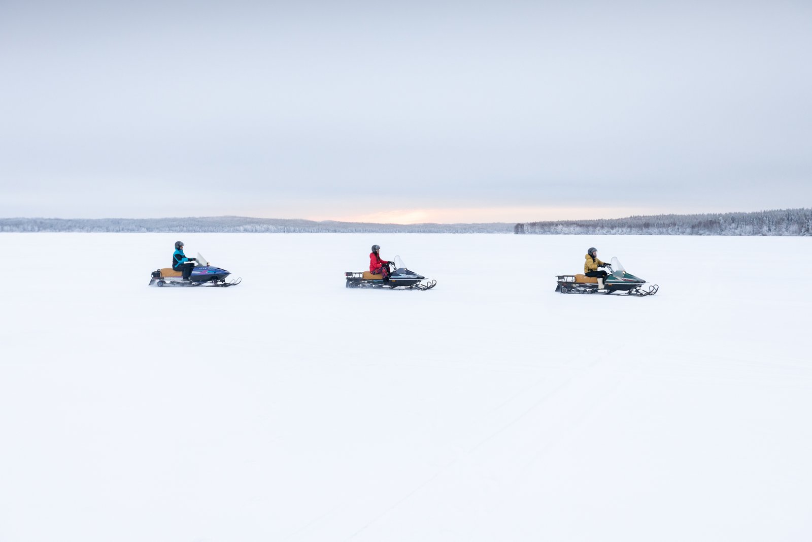 Three snowmobiles in single file on a frozen lake.