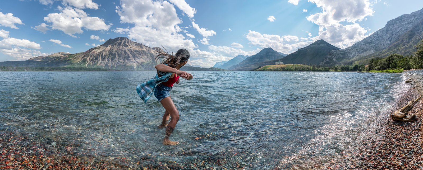 Person with feet in the water skipping rocks into lake in Waterton Lakes National Park.