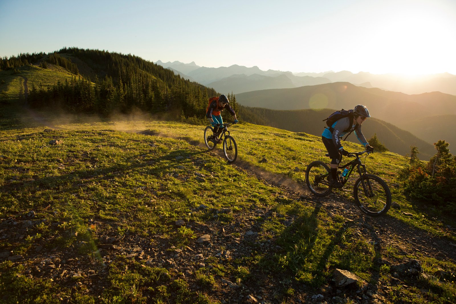 Two people mountain biking over hills during sunset.