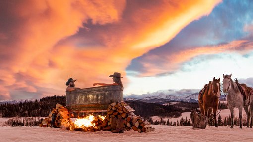 Couple in outdoor rural hot tub in winter during a sunset with horses in the background.