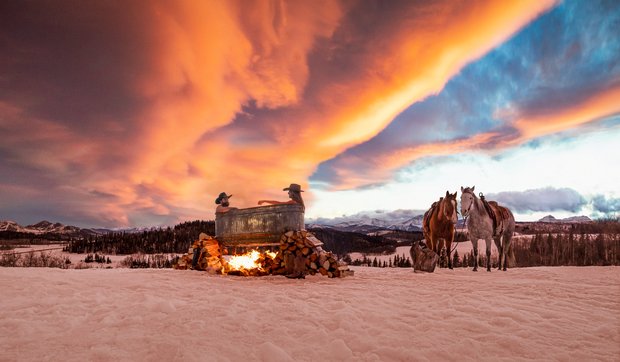 Couple in outdoor rural hot tub in winter during a sunset with horses in the background.