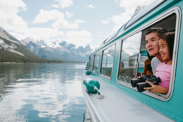 Man and child looking out the window of a boat on Maligne lake with binoculars.