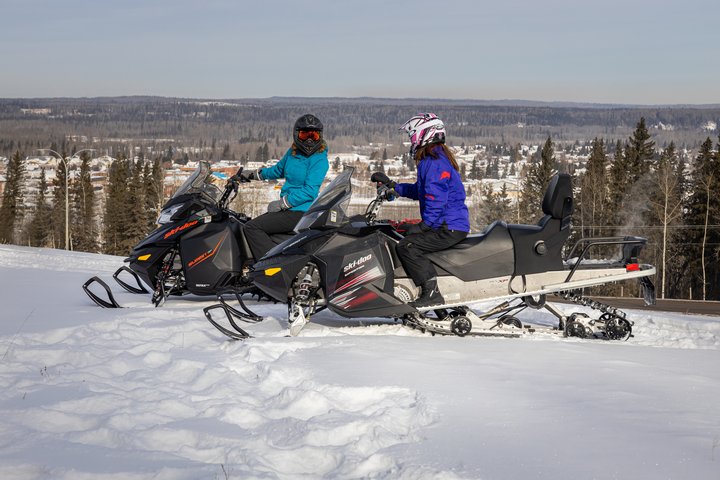 Two people on snowmobiles stop to chat before snowmobiling on a winter's day.