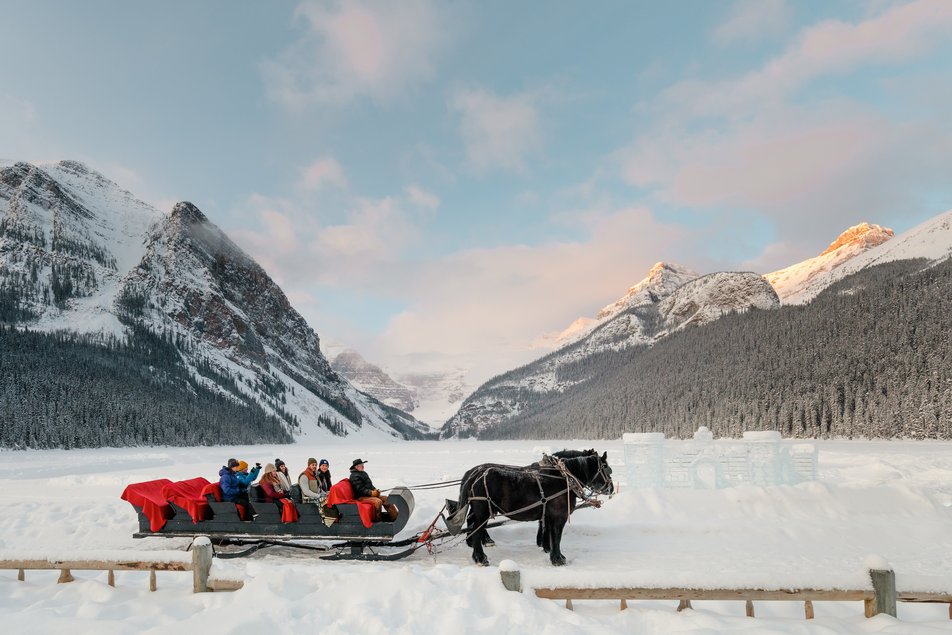 A group enjoys a sleigh ride along a frozen Lake Louise, ice sculptures and mountains in the background in Banff National Park