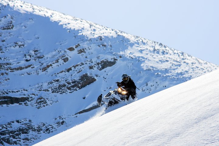 A person snowmobiling down a hill on a sunny blue-skied winter's day.