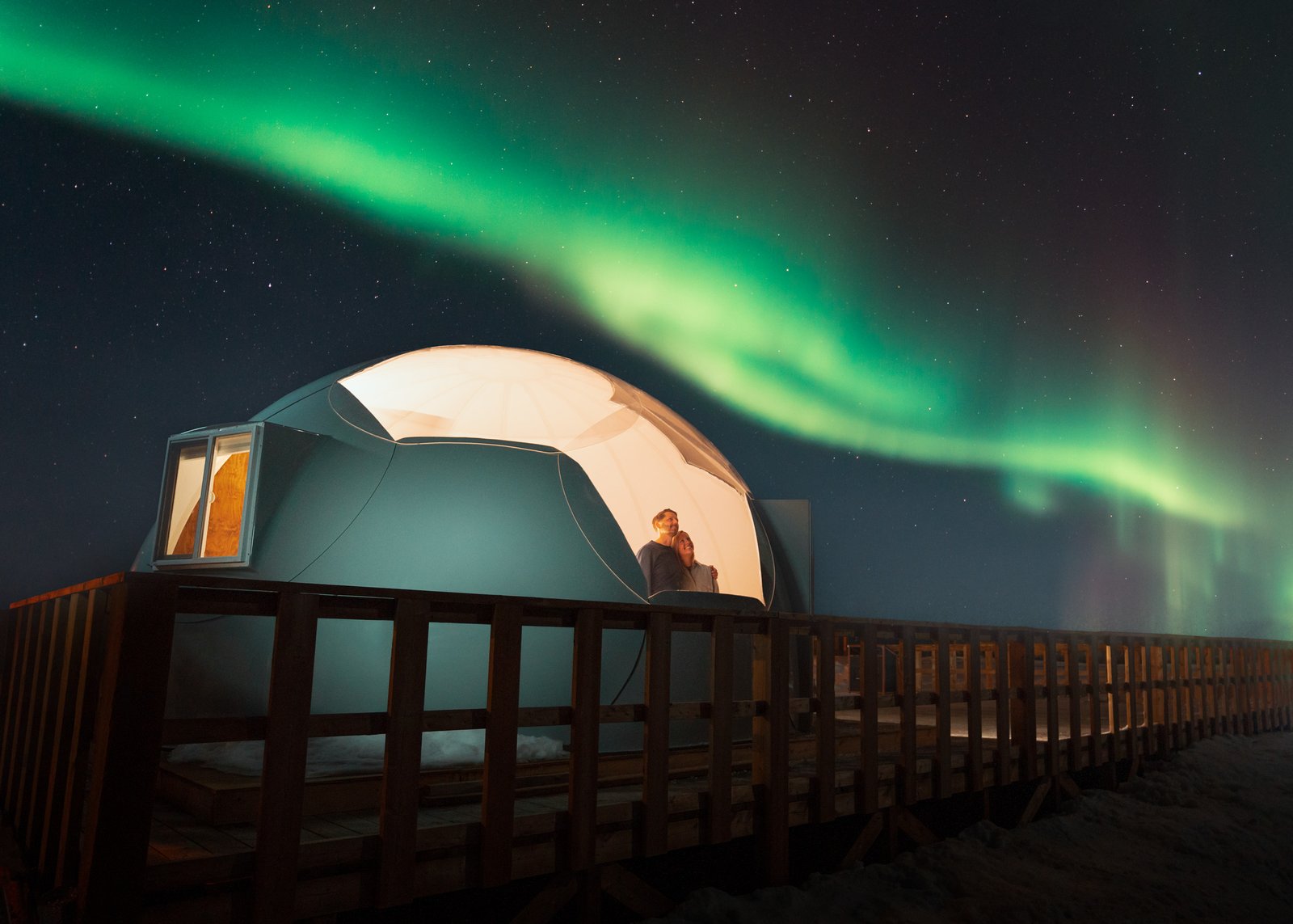 A couple in an embrace looking up at Northern Lights from inside a yurt.