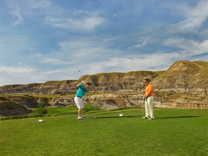 Two men golf on a course in the badlands.