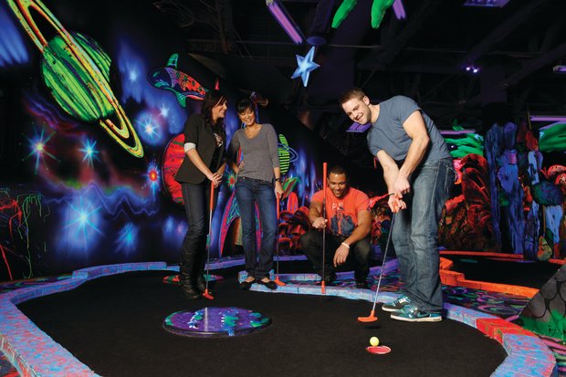 Group of four smiling while they play glow in the dark mini golf.