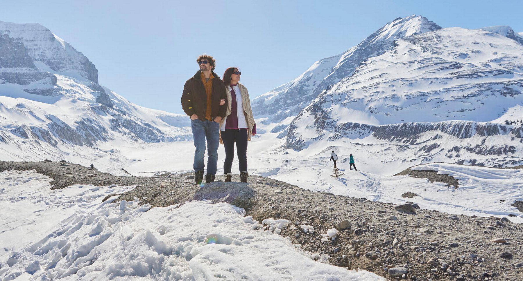 Young couple walking on a rocky path at the Columbia Icefields on a sunny blue sky day.