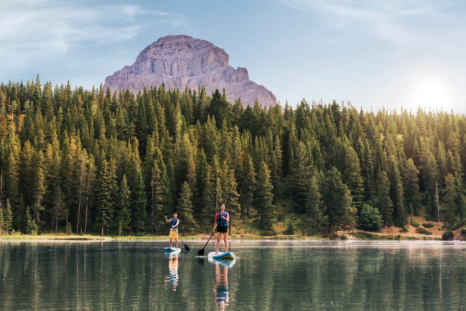 Couple paddleboards on a lake with a mountain and trees in the background.