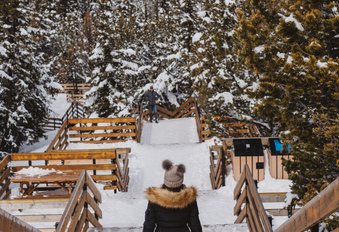 A visitor in a fur-lined parka walks the snowy boardwalk at the top of the Banff Gondola in Banff National Park.