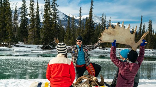 Four people sitting by a river in the winter learning about antlers from a guide.