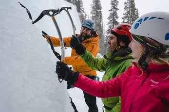 An ice climbing guide teaches travellers how to use ice climbing axes at the base of frozen Tangle Falls in Jasper National Park.