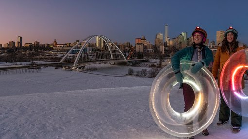 People tubing down snow hills with the Edmonton skyline and Walterdale Bridge in the background.