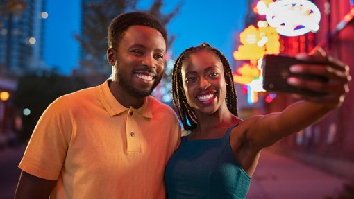 Couple taking a selfie on the street at night with neon signs in the background.