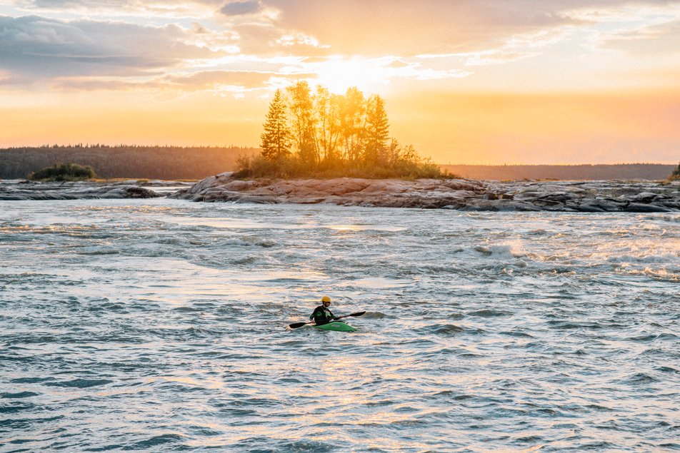 Kayaker navigates rapids with island in the background.