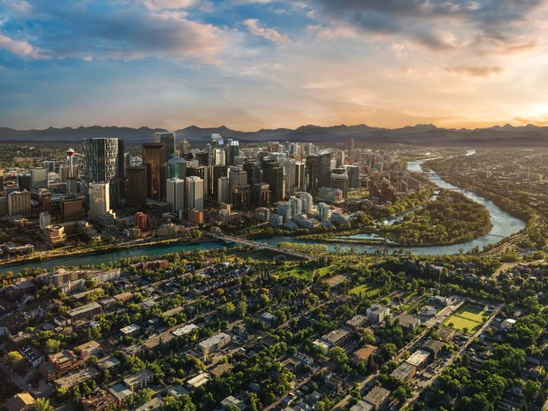 Aerial shot of the Calgary Downtown and surrounding areas with the Rocky Mountains in the distant background on a sunny evening.