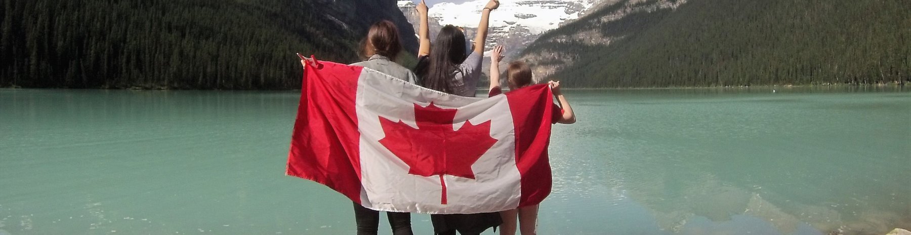 Group of friends holding the Canada / Canadian flag at the edge of a lake with mountains in the distance
