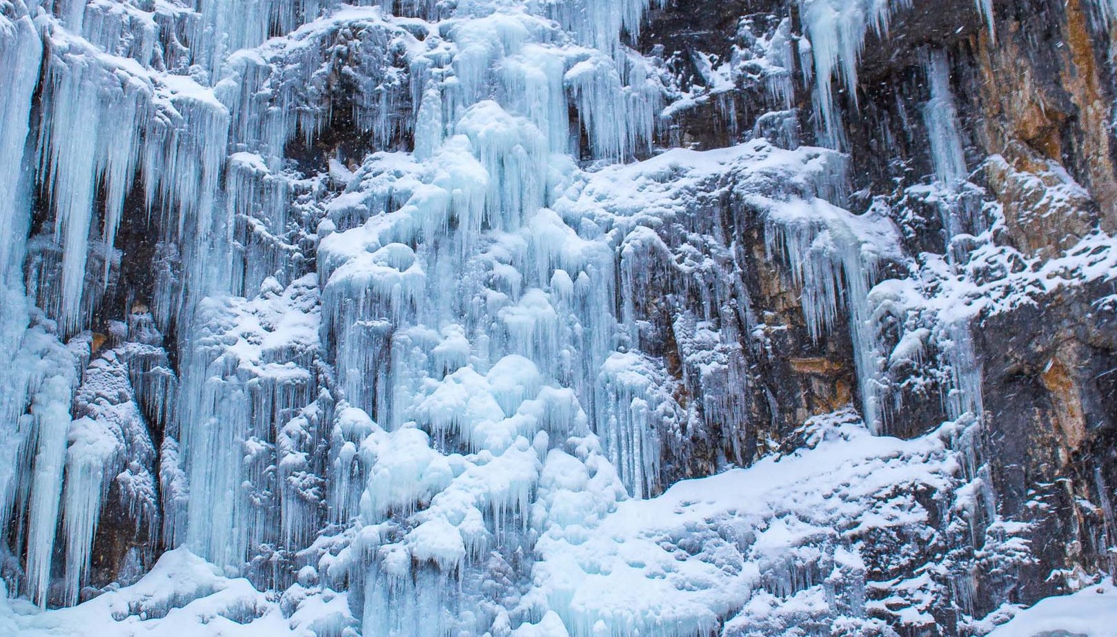 Two hikers looking up a frozen waterfall in Waterton National Park.