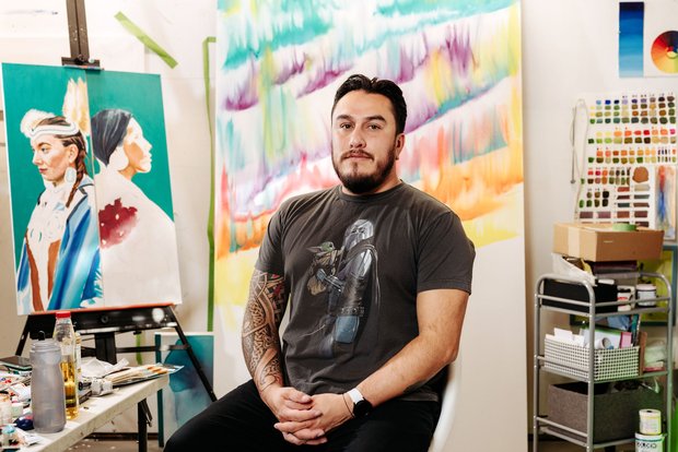 Man sitting in an art studio with colourful paintings behind him.