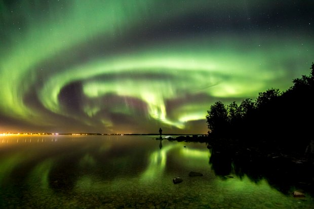 Person standing on the banks of Cold Lake watching the Northern Lights.