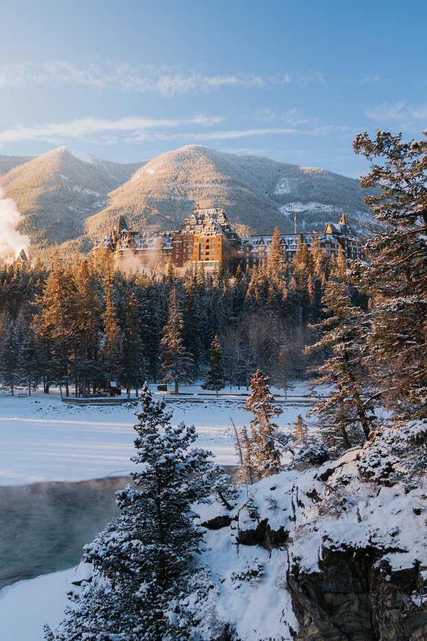 Historic hotel in the distance surrounded by a forest with a mountain view in the background during winter.
