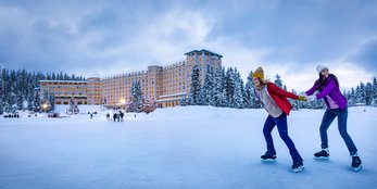 One person pulling another while skating on Lake Louise with the Fairmont Château Lake Louise in the background.