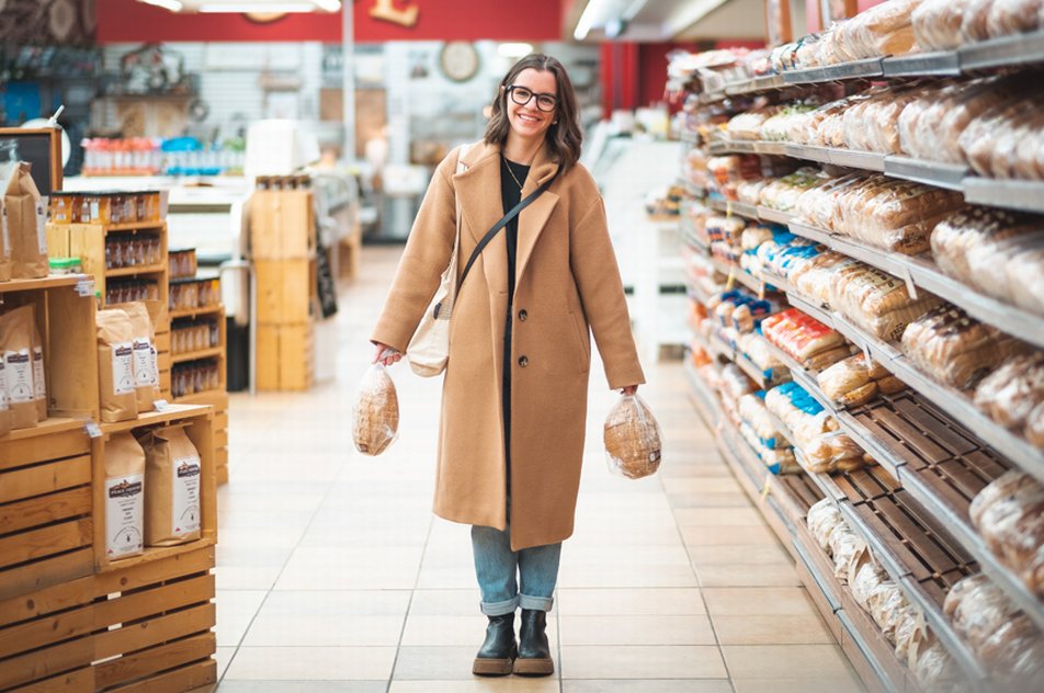 Woman standing in a grocery store holding two loaves of bread.
