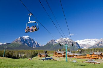 People riding a chairlift in the summer with views of the lodge building at Lake Louise
