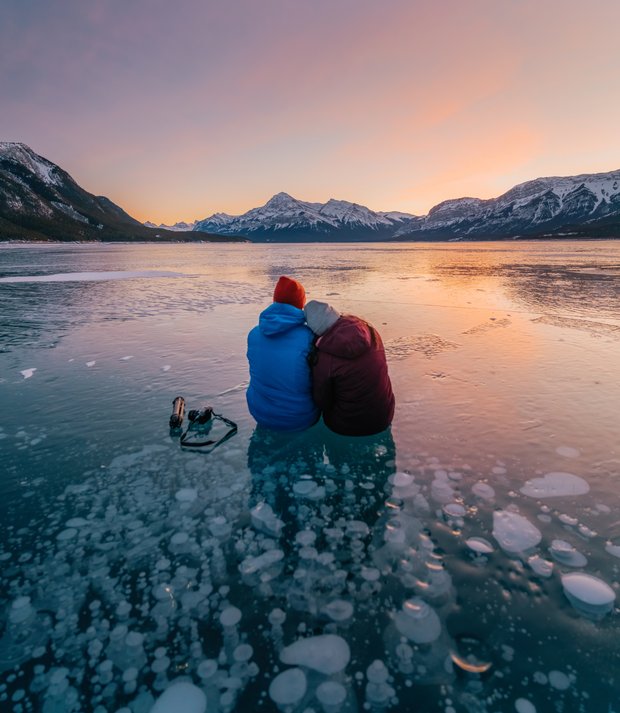 A couple sit on the methane bubbles under a frozen lake while admiring the sunset.