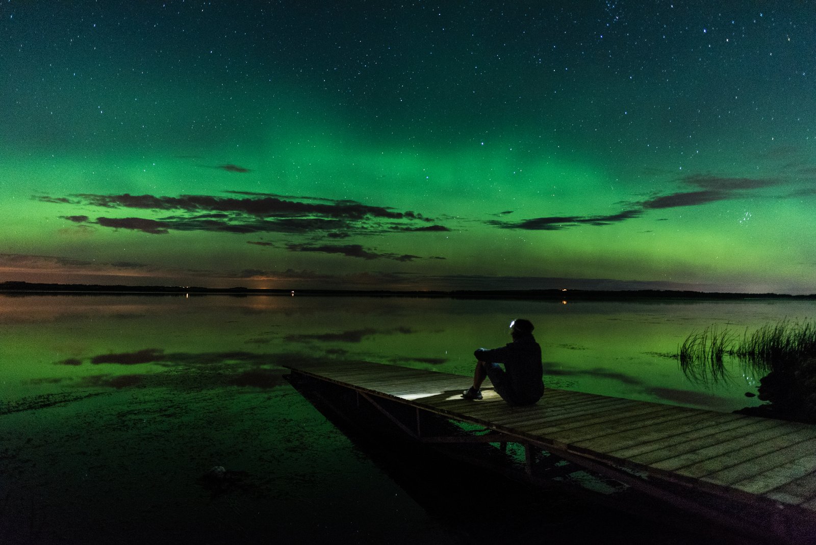 A person sitting on a dock admiring the northern light sky in Grande Prairie.