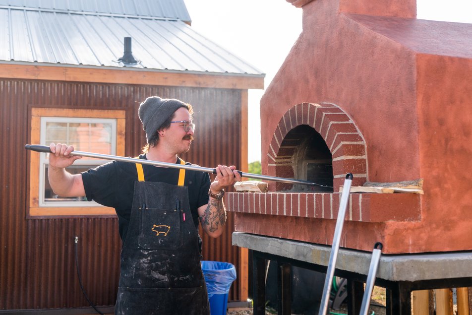 A man cooks a dish in a brick oven.