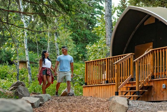 A couple goes for a walk down the pathway past the lodge at Glamping Resorts in Castle Provincial Park.