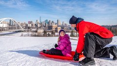 A dad gets ready to push his child down a tobogganing hill at the Indigenous Art Park in Edmonton.