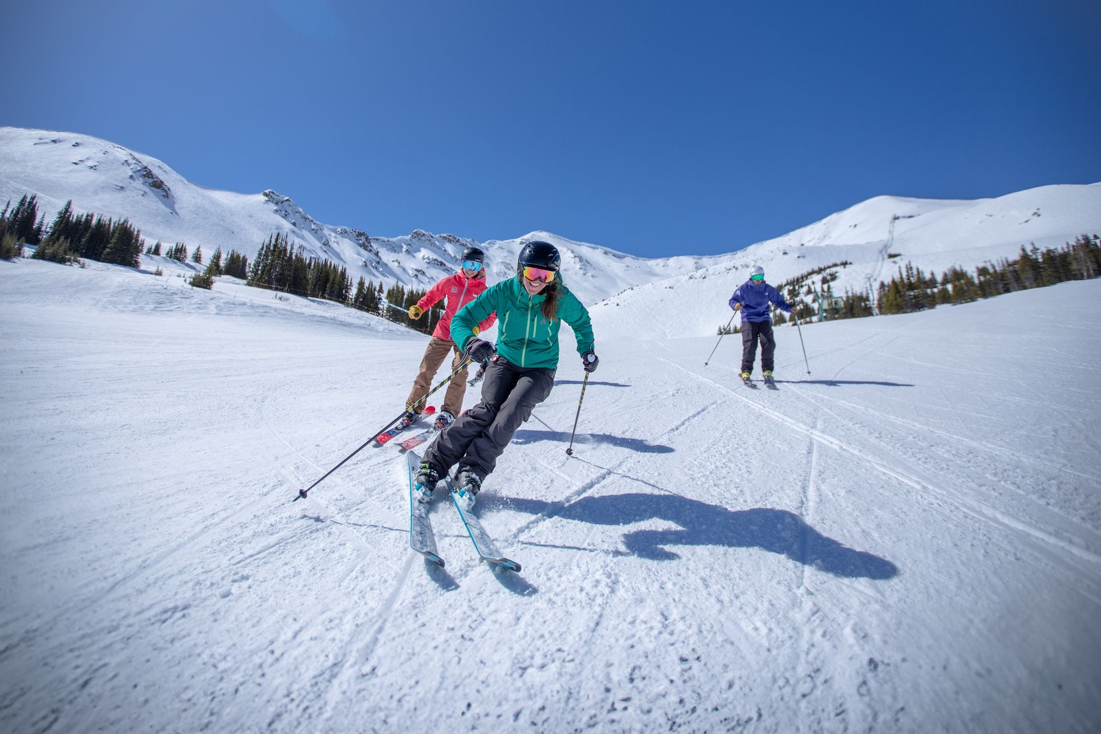 Three skiers front-on, skiing a groomed run at Marmot Basin in Jasper National Park.